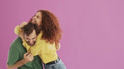 Sticker - Beautiful happy young couple having fun and playing with hair while hugging over pink background isolated