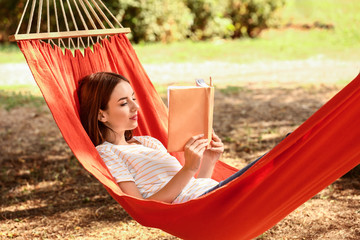 Poster - Beautiful young woman with book resting in hammock outdoors