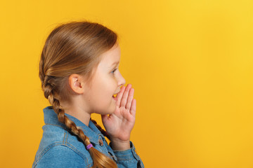 Child profile side view. The little girl speaks aside, holds a hand at a mouth