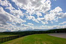 Landscape Of Green Grass With Fence, Big White Clouds,  Blue Sky, And Mountain Lines From Far Away In The Back - Hokkaido, Japan