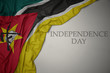 waving colorful national flag of mozambique on a gray background with text independence day.