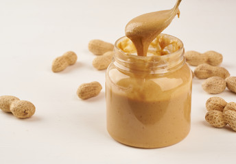 jar of peanut butter and peanuts in shell on a white table, side view, fresh ground crushed nuts, side view