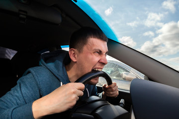 An unbalanced, goosey man bites a car steering wheel from anger while driving in a traffic jam or after an accident. A nervous and nutty guy cannot restrain his emotions and yells at other road users.