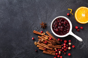 Cranberry sauce in ceramic saucepan with ingredients for cooking on stone black table top view.