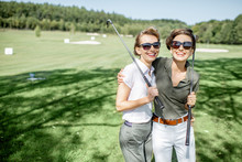 Portrait Of A Two Female Best Friends Standing With Golf Equipment On A Playing Course, Talking And Having Fun During A Game On A Sunny Day