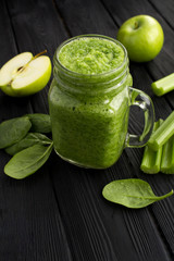 Wall Mural - Green smoothies with spinach, apple and celery  on the black wooden background. Location vertical. Copy space.