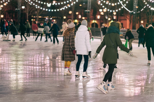 group of girs skating back to us. girlfriends ice skating in city park, snowy evening. healthy outdo