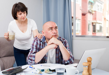 Worried man working at laptop and financial documents, woman helping