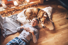 Boy lying on the floor and near beagle dog sleeping on sheepskin in cozy home atmosphere