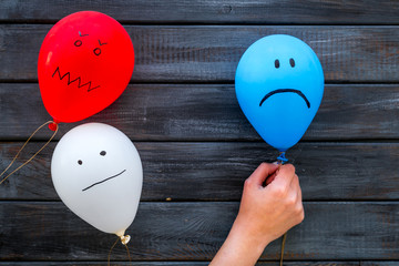 Wall Mural - Negative emotions concept. Balloons with drawn faces on dark wooden background top view copy space