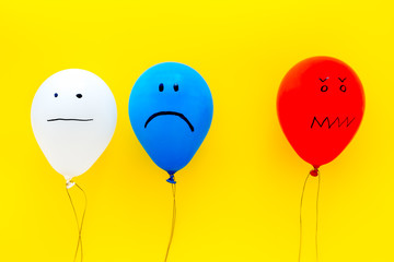 Wall Mural - Negative emotions concept. Balloons with drawn faces on yellow background top view