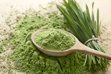 Wooden spoon with wheat grass powder and green sprouts on table