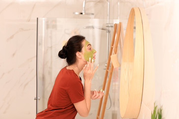 Sticker - Young woman applying mask on her face near mirror in bathroom