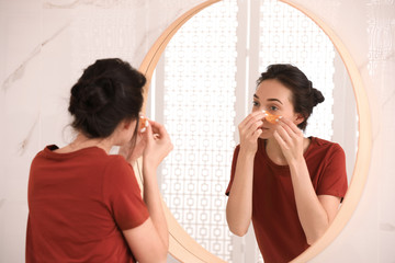 Sticker - Young woman with eye patches near mirror in bathroom