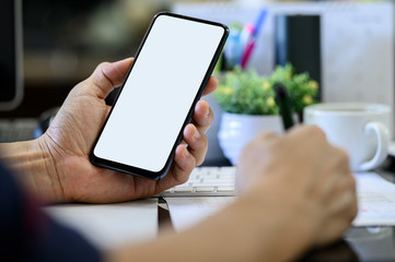 Wall Mural - closeup man hand holding smartphone with blank white screen while working at office desk.