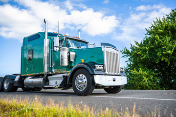 Green classic big rig semi truck tractor driving on the road in Columbia Gorge for pick up loaded semi trailer