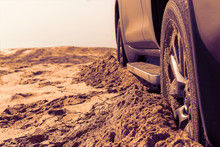 Car Wheels On A Sea Beach Sand. Close-up Of Car Wheel On Sandy Dunes. Car Stuck In The Sand. Spinning Wheel Of A Car Stuck In The Sand.