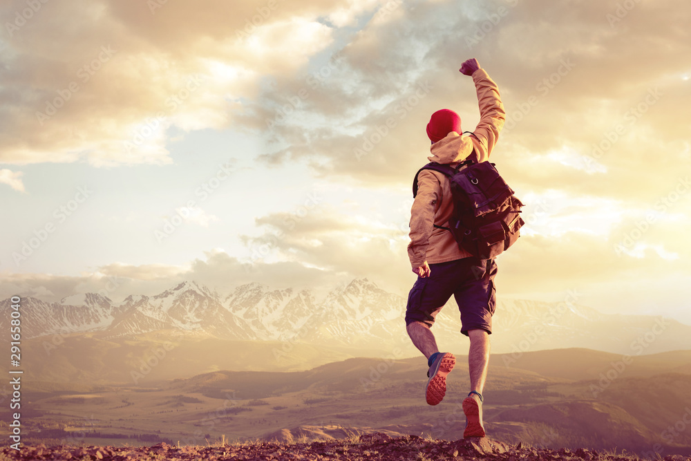 Happy man jumps in winner pose against sunset mountains - obrazy, fototapety, plakaty 