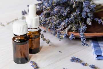 Two glass bottles with cosmetic oil in it and lavender flower behind on a white wooden table