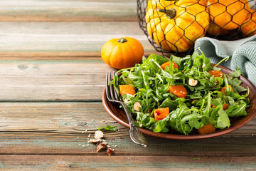 Wall Mural - Delicious salad with arugula, baked pumpkin, hazelnut and sesame seeds on brown plate. Paleo diet food concept with copy space.