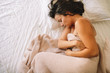 © JustLife - Young woman having stomachache lying on white bed