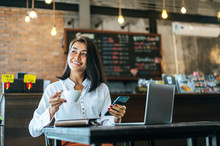 Woman Sitting Happily Working With A Smartphone In A Coffee Shop And Notebook.