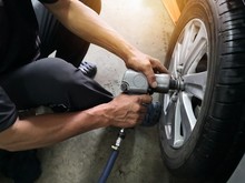 Removing Car Mechanic To Repair The Leaky Tire Car Wheels.Mechanic Changing A Car Tire On A Vehicle A Hoist Using An Electric Drill To Loosen The Bolts .concept Of Service Or Replacement.