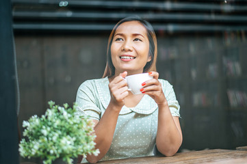 The young woman happily drinks coffee in the coffee shop.