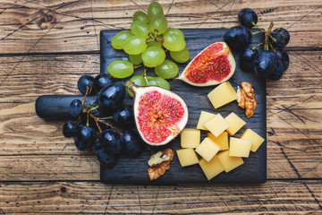 Wall Mural - Cheese cubes, fresh fruit figs grapes Honey walnut on wooden chopping Board. Selective focus. Close up.