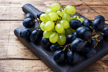 Wall Mural - Clusters of black and green grapes Kish Mish on a wooden Board. Copy space.