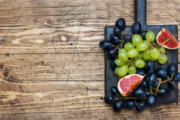 Wall Mural - Clusters of black and green grapes Kish Mish and figs on a wooden Board. Copy space.