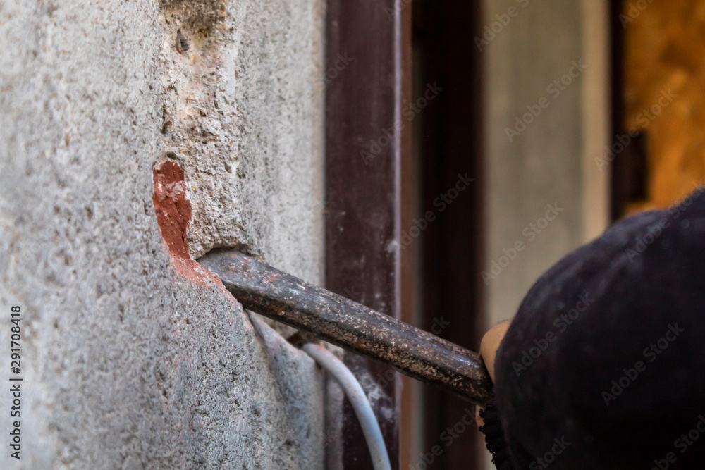 Man Making Hole in Wall to Install Ring Doorbell Using Metal Spike For Concrete - obrazy, fototapety, plakaty 