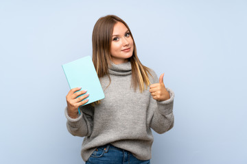 Teenager girl with sweater over isolated blue background holding and reading a book