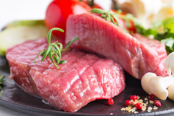 Poster - Raw beef steak on the bone with fresh vegetables in a pan on a marble background, top view