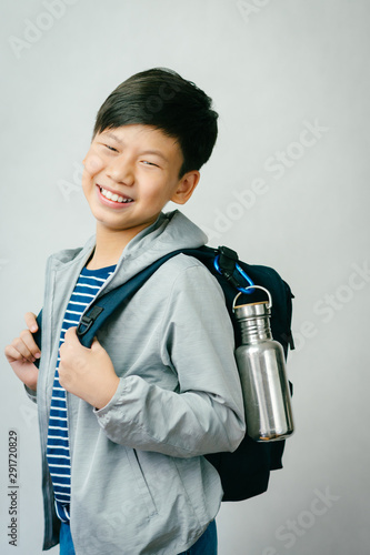 Eco friendly living concept. Happy and smart looking Asian preteen boy smiles and carry navy blue backpack with his reusable stainless steel water bottle to school. Sustainable lifestyle.