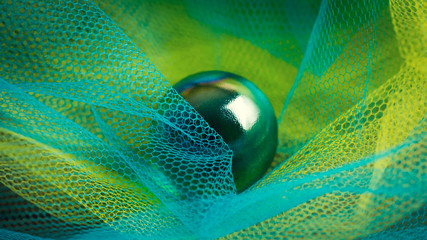 Dark green glass sphere in the yellow and blue plastic fishnets. Abstract high resolution macro photography with 16:9 proportion for web design and decor.