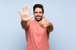 © luismolinero - Handsome young man in pink shirt over isolated blue background counting six with fingers