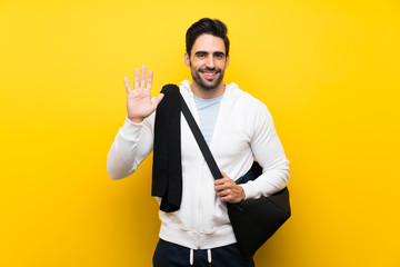 Wall Mural - Young sport man over isolated yellow wall saluting with hand with happy expression