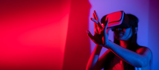 Young woman using glasses of virtual reality on dark background. Smartphone using with VR headset,virtual reality,future technology concept.Asian woman using VR glasses in colorful neon lights.