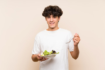 Young man with salad over isolated green wall