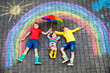 © Irina Schmidt - three little children, two school kids boys and toddler girl having fun with with rainbow picture drawing with colorful chalks on asphalt. Siblings in rubber boots painting on ground playing together.