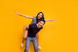 © deagreez - Photo of cheerful crazy couple of friends with girl pretending to be airplane and guy holding her on back while isolated with yellow background
