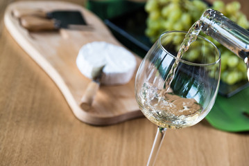 Wall Mural - Pouring white wine into the glass against wooden background