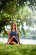 © chika_milan - Smiling Caucasian woman in sports clothing sitting on mat in nature and meditating.