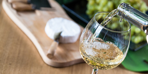 Wall Mural - Pouring white wine into the glass against wooden background