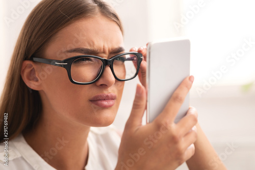 Fotografía Girl Looking At Cellphone Through Eyeglasses Having Vision Problem Indoor