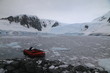 czerwony ponton przycumowany do skalistego brzegu w zimnej zatoce pokrytekj krą i ośnieżone góry w tle