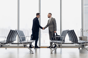 Full length side view of businessmen shaking hands in airport terminal