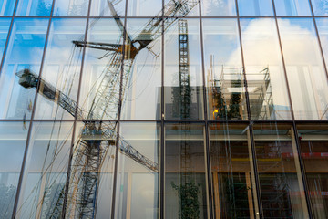 Reflections of a frane and construction site in the glass facade of an office building.