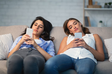 Two Girls Using Smartphones Sitting On Couch Indoor